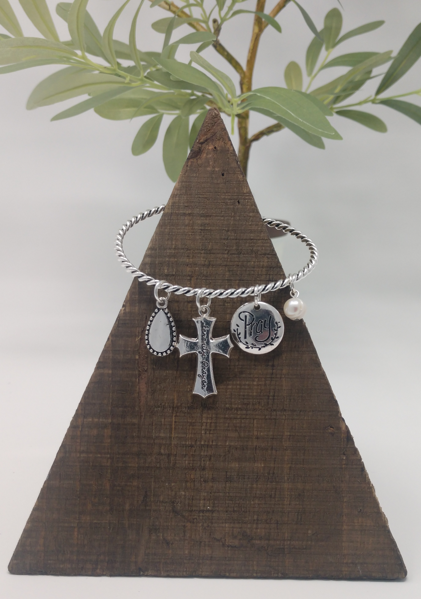 This bangle bracelet is made of a twisted silver tone band a 1.25" serenity prayer cross, .75" Pray disc charm, .75" teardrop charm, .5" faux pearl charm. It measures approximately 2"-2.5" in diameter. They close with a well designed hook closure.