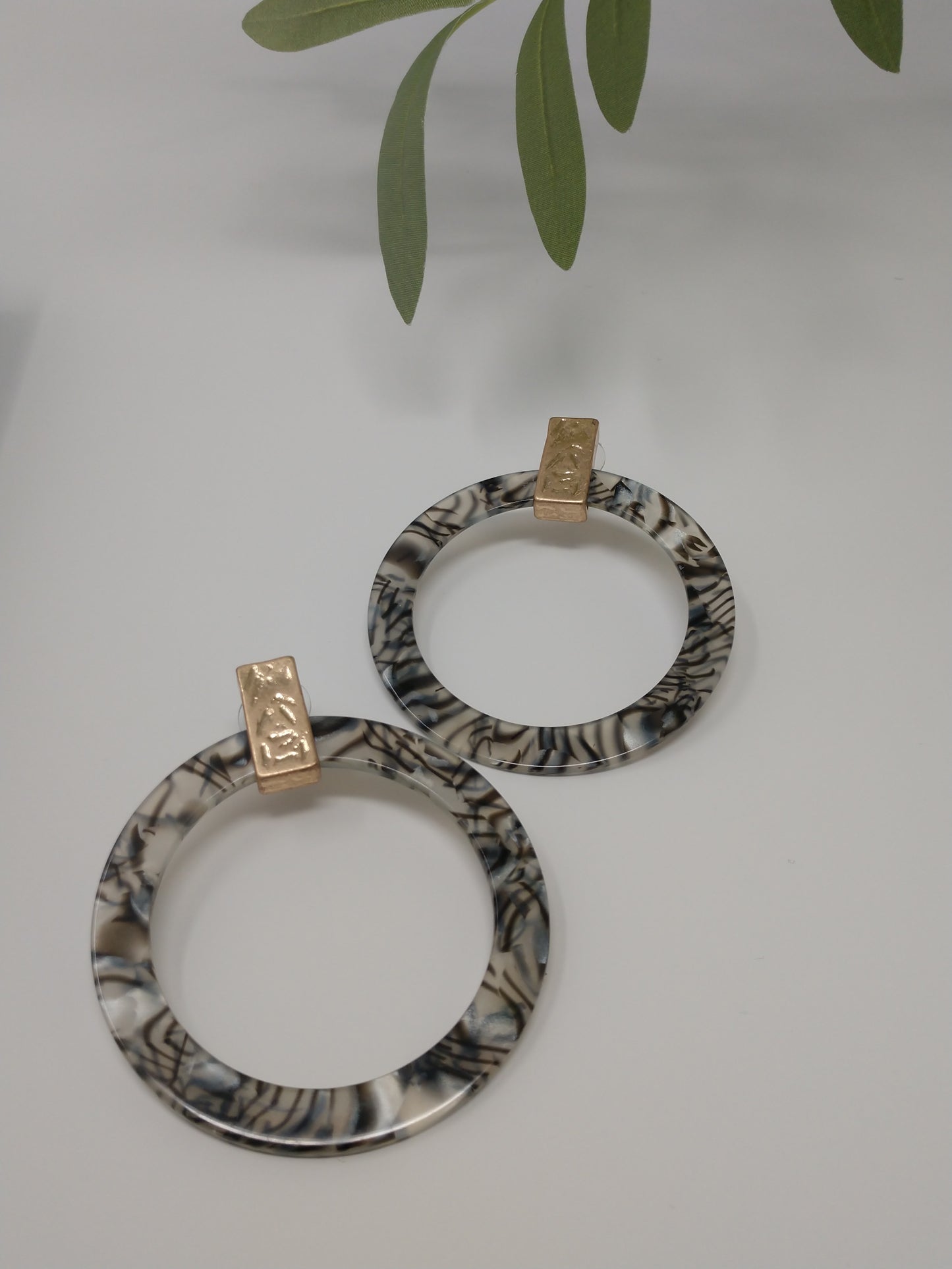 These hoops are a statement piece. They are a gray marbled print resin with a gold tone accent piece at top of earring. They are flat hoops and measure 2.75" and are a post style.