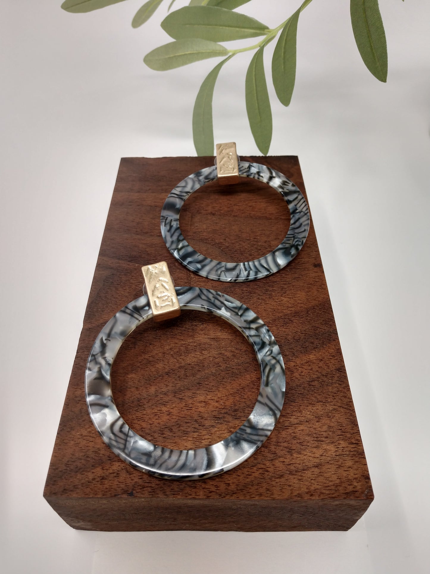 These hoops are a statement piece. They are a gray marbled print resin with a gold tone accent piece at top of earring. They are flat hoops and measure 2.75" and are a post style.