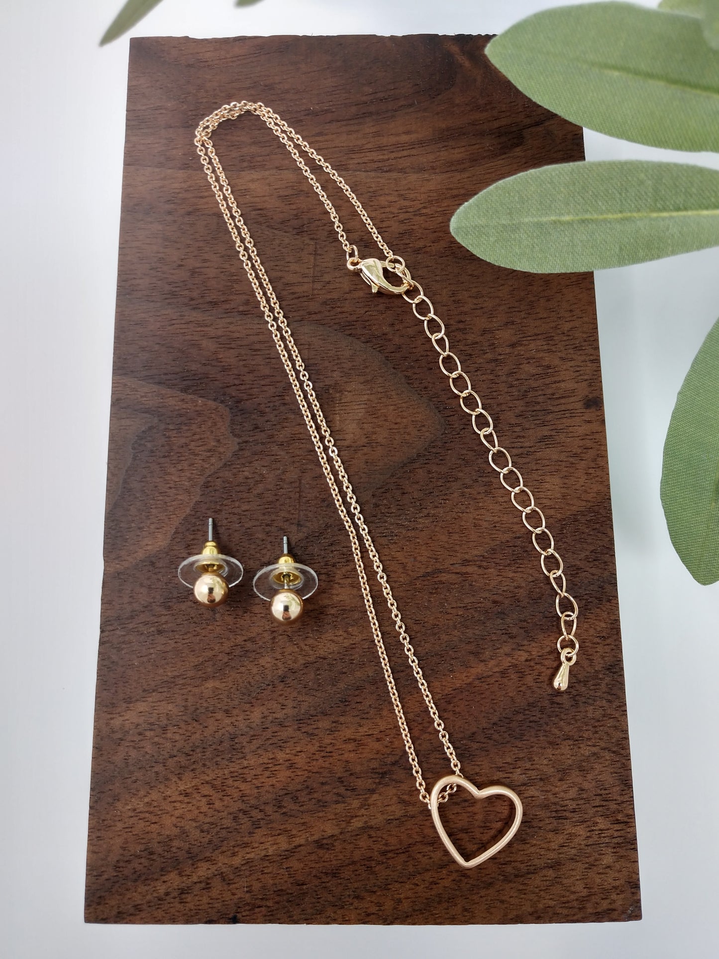 It is a 15" long worn gold tone chain with a 3" extender. The worn gold tone heart pendant measures approximately .5" and has a lobster claw closure. Plus, it comes with cute .25" post style earrings to match.