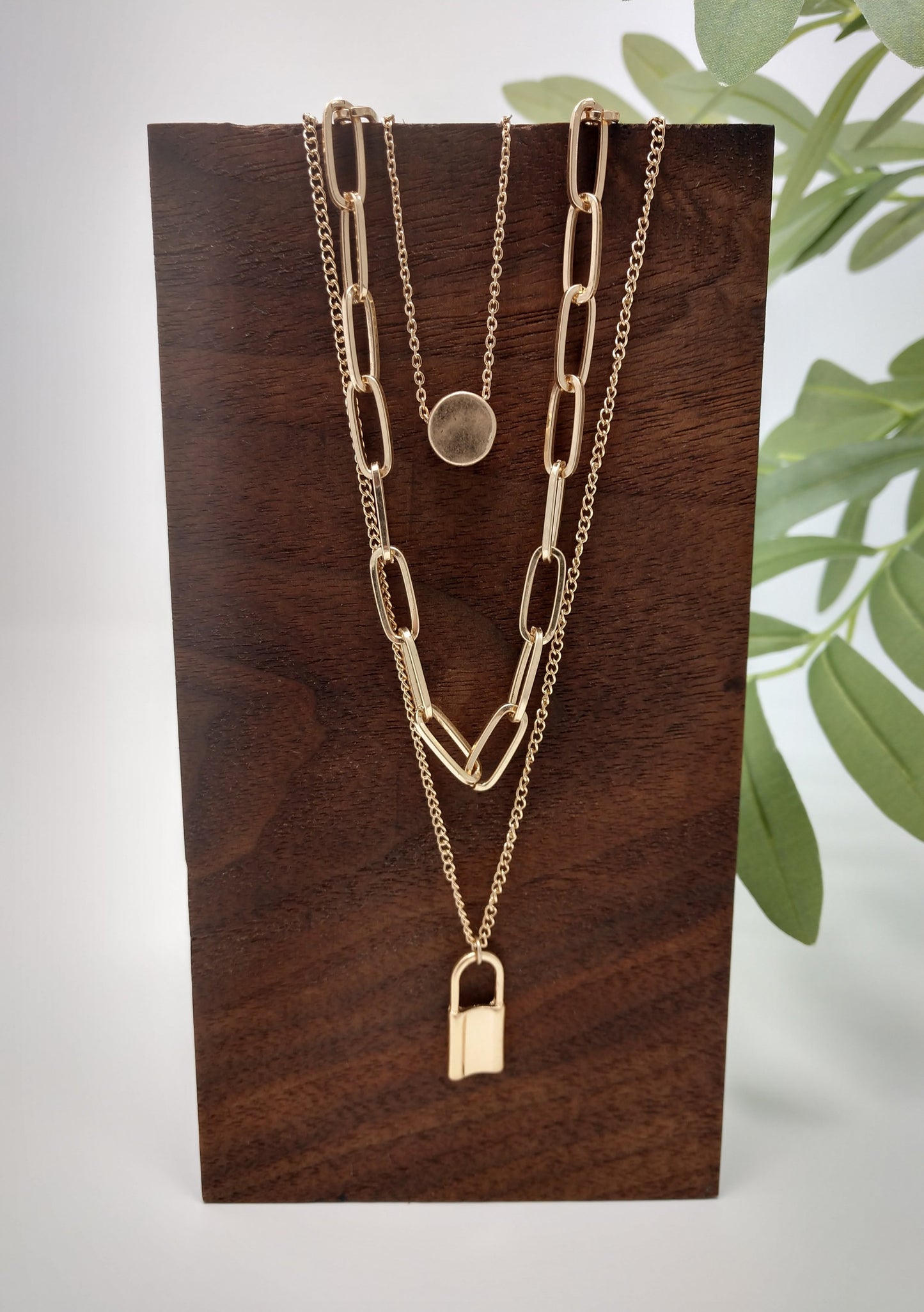 Padlocks are so popular right now and this three stranded necklace is such a great piece. It would make a great gift for the hard to buy for teen or for your trendy self! It is a 16" long chain with a 3" extender and a disc pendant, a 20" long middle linked chain, and a 24" bottom chain with padlock. The worn gold tone gives it a unique look and the padlock and disc pendants measure up to .75". Lobster claw closure.