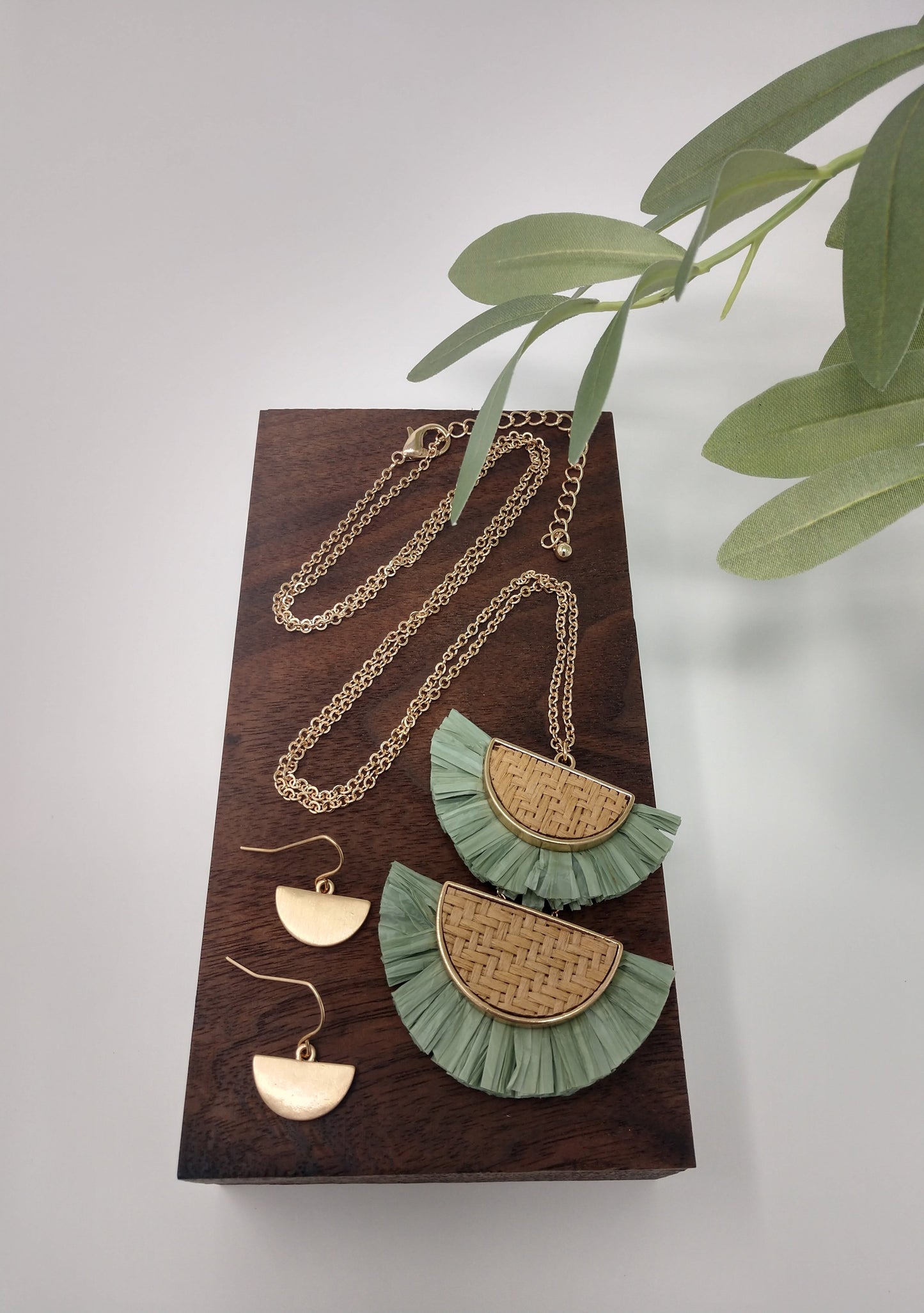 It is a 30" long gold tone necklace with a 3" extender and lobster claw closure. It is made with rattan, and raffia material. The pendant measures 2.5" and is so delicate feeling. Plus, it comes with the most perfect set of earrings. They are .75" fish hook style with a .25 drop. Fashion jewelry is a great way to add affordable fun, colorful, trendy pieces to your collection.