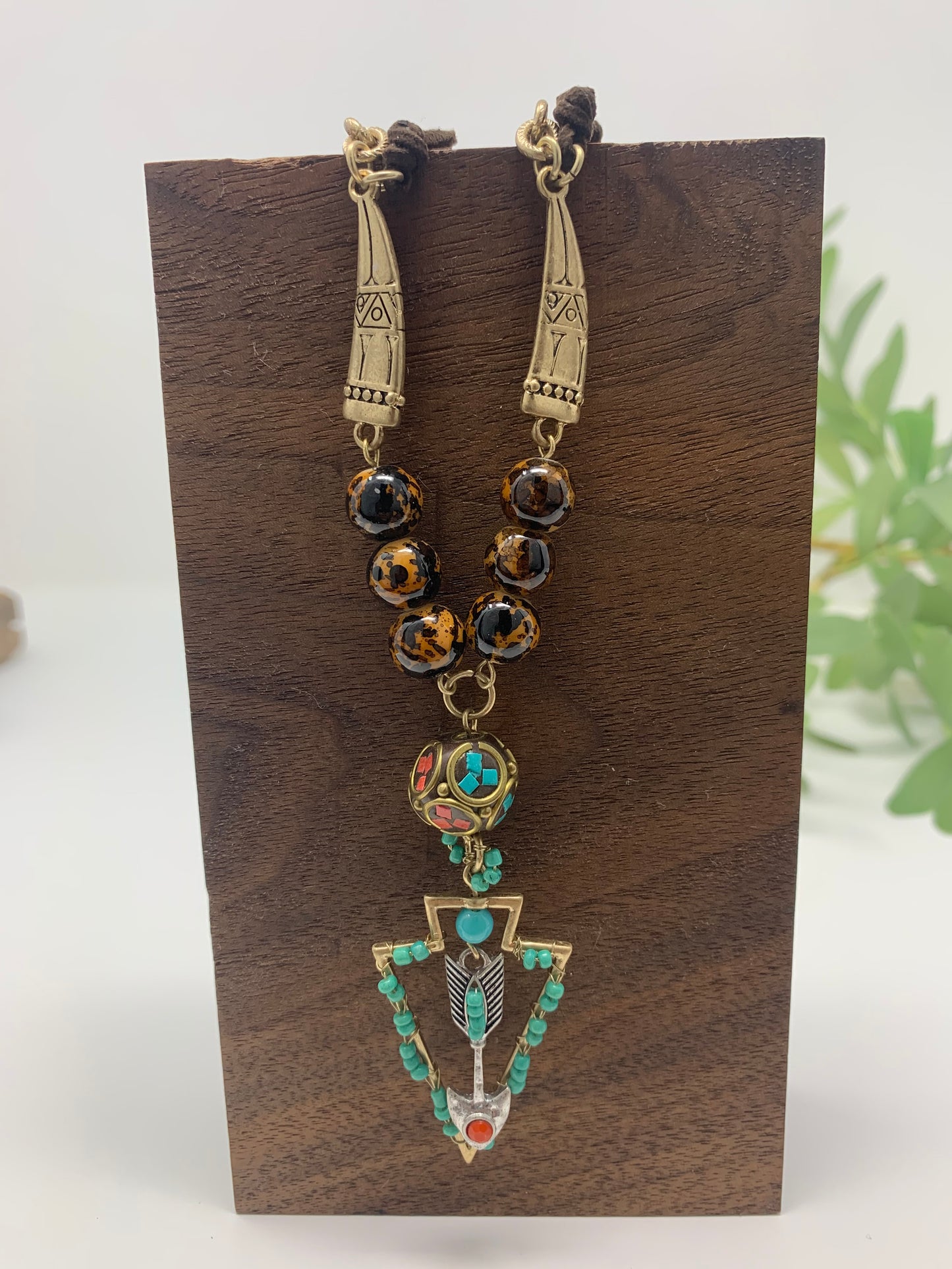 Fashion jewelry. The necklace measures 14.6" with a 2" extender and matching arrowhead earrings. Gold tone chain with brown rope connects to two engraved goldtone charms that connect to faux tiger eye beads and a unique bead with bright teal and read accents. The arrow head pendant is goldtone with turquoise colored beads and has a silver tone arrow with turquoise and red colored stones. Earrings match the pendant except they have leather cord instead of silver tone arrow.