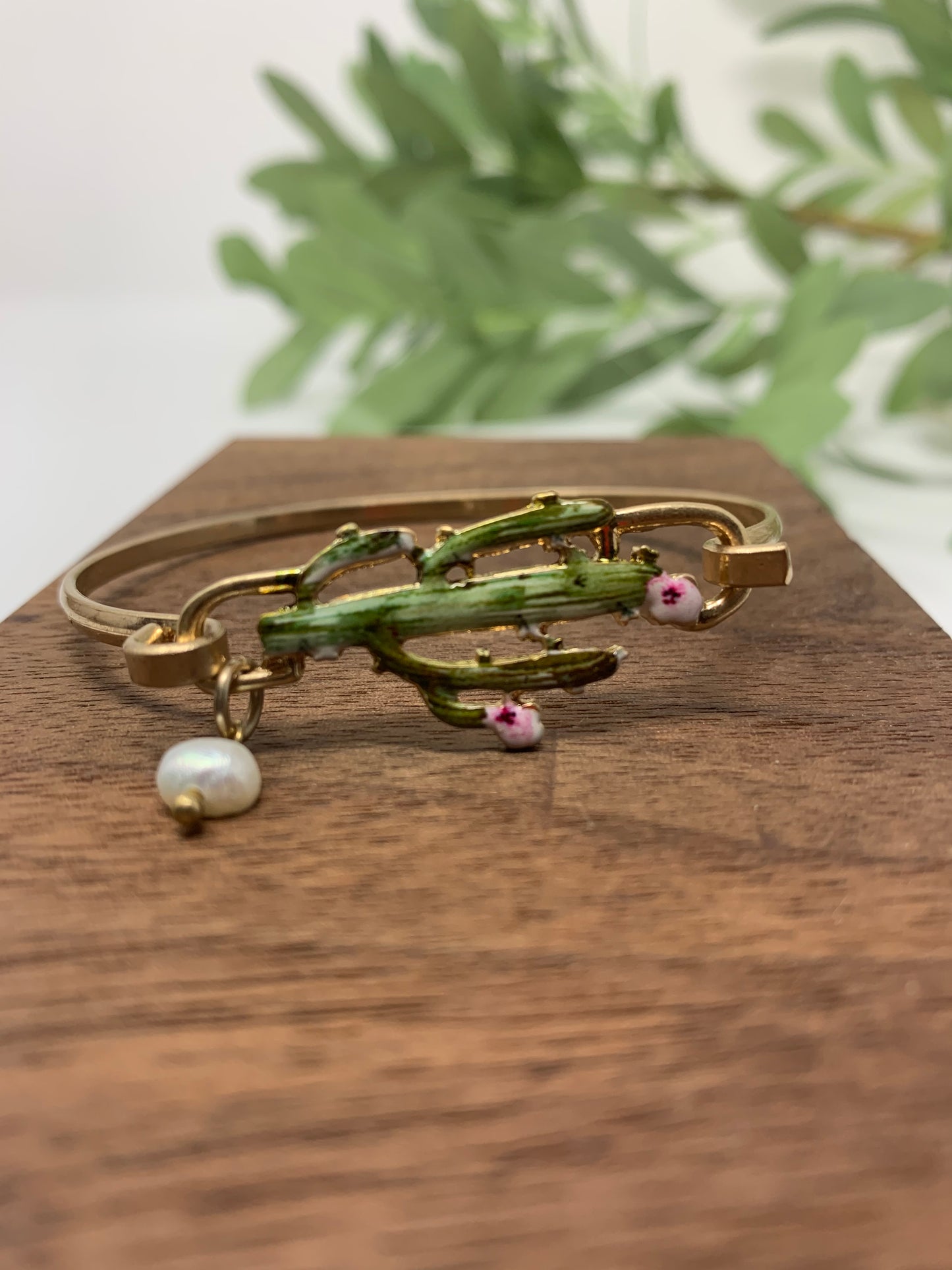 Gold tone bracelet with cactus that is colored perfectly. Wire bracelet closes with a hood closure and a faux pearl charm to add a touch of fancy.
