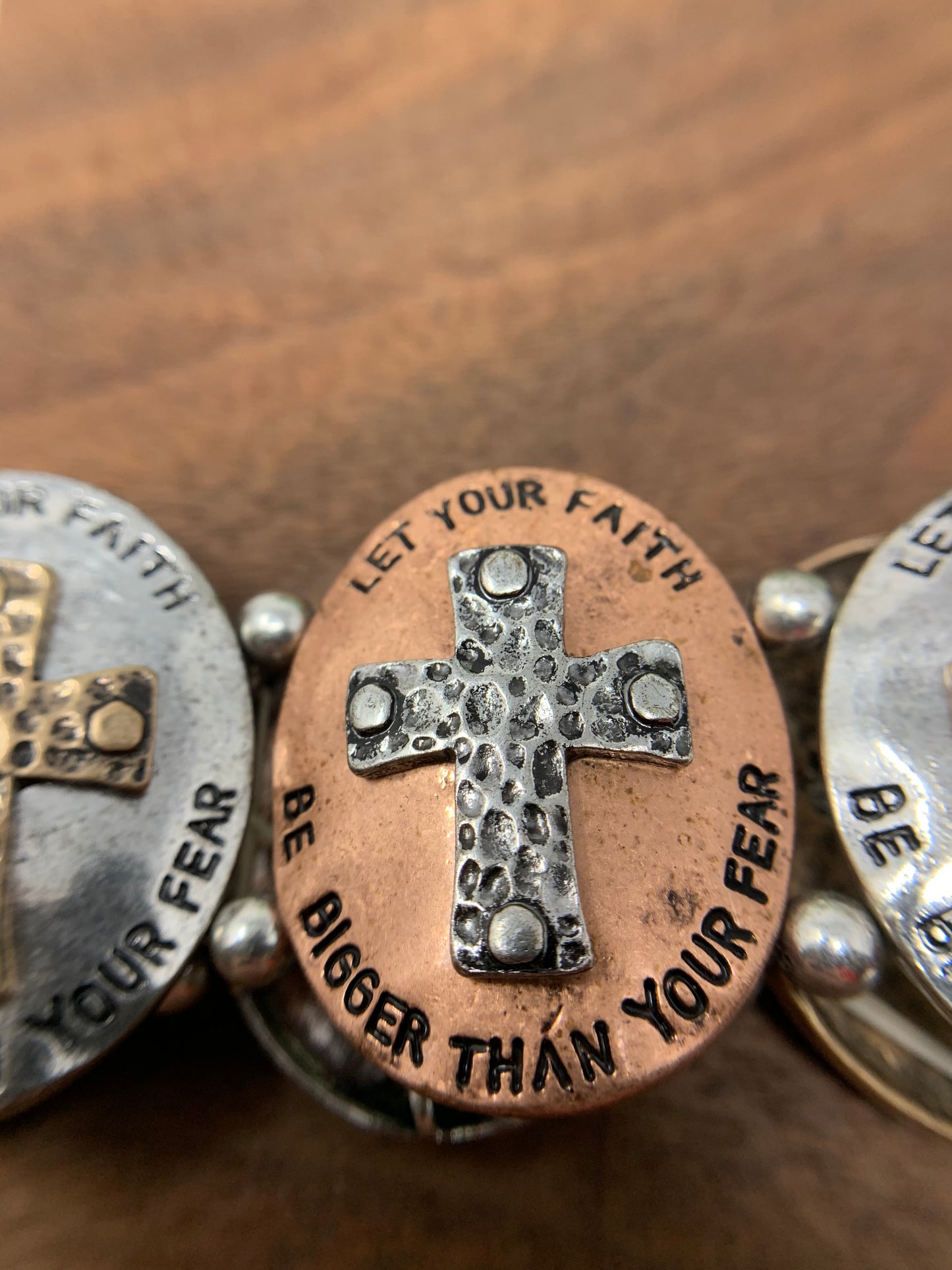 This stretch bracelet has six oval shapes with crosses and engraved with "LET YOUR FAITH BE BIGGER THAN YOUR FEAR" around each cross. Ovals are in bronze tone, gold tone, and silver tone.