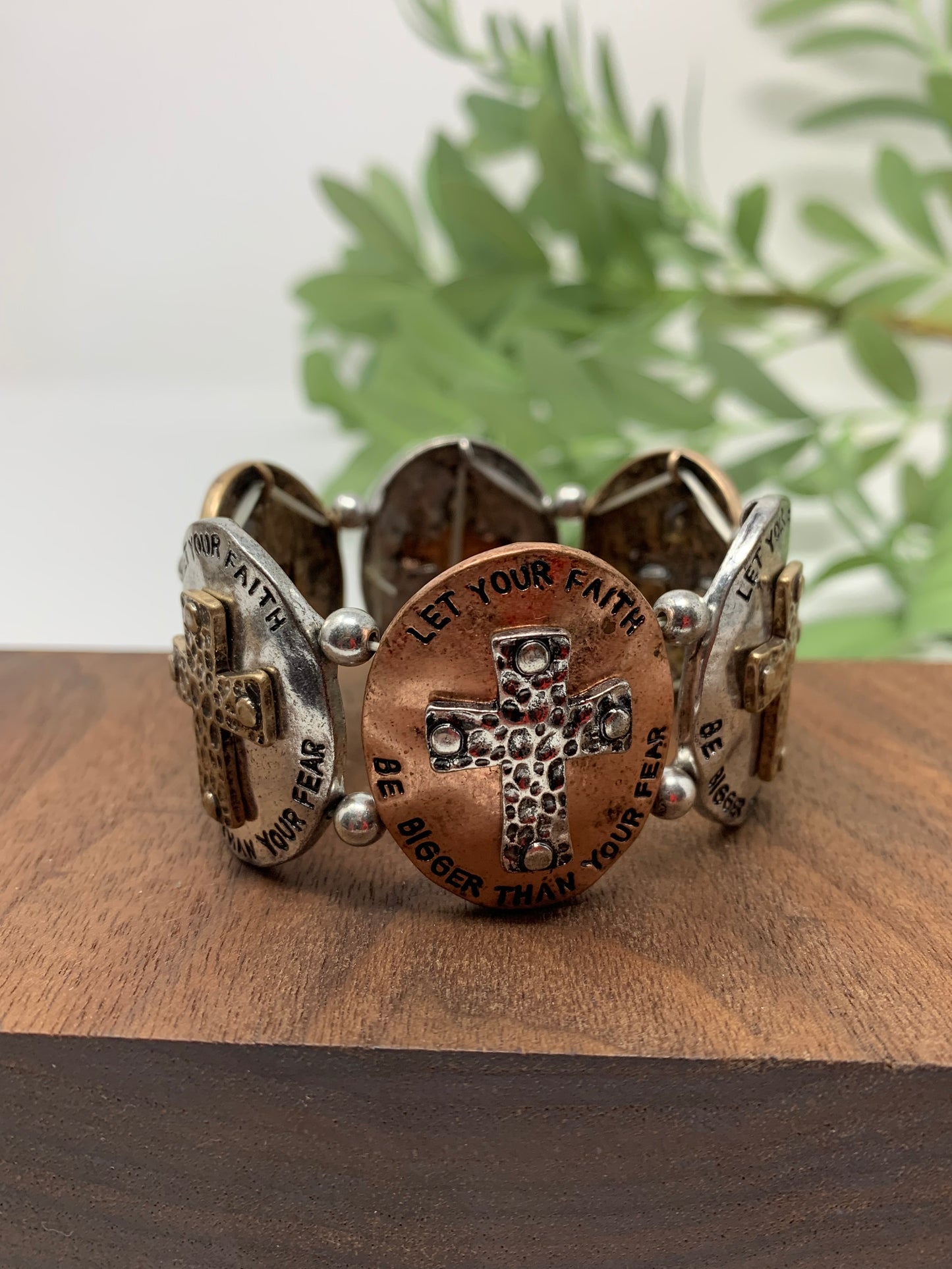This stretch bracelet has six oval shapes with crosses and engraved with "LET YOUR FAITH BE BIGGER THAN YOUR FEAR" around each cross. Ovals are in bronze tone, gold tone, and silver tone.