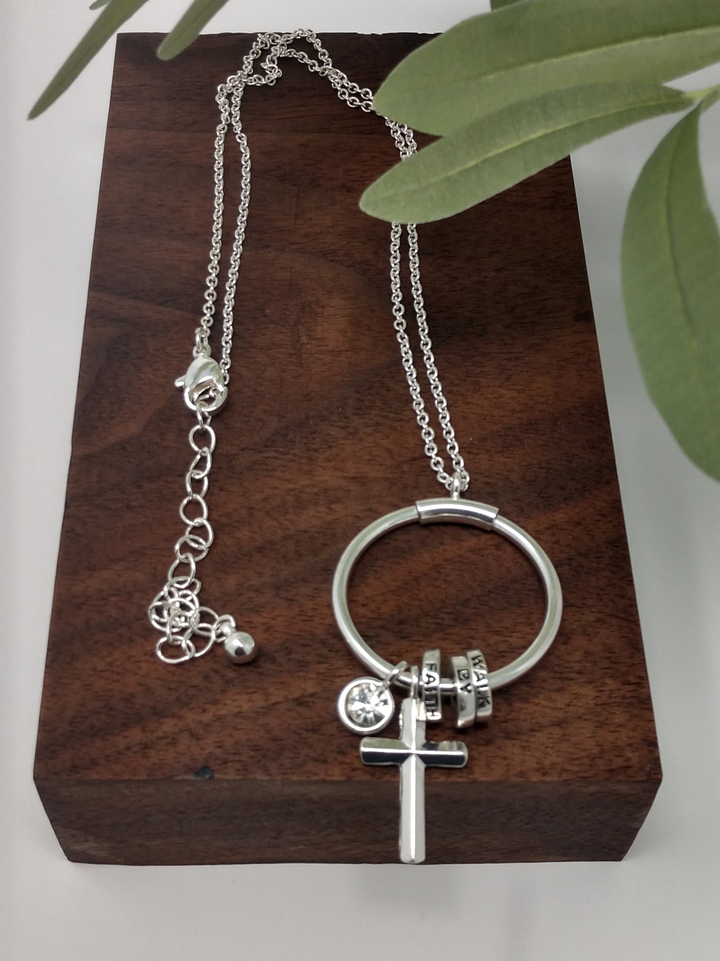 This antique silver tone necklace is 18" with a 3" extender with a lobster claw closure. It is beautifully finished with a 2.5" ring pendant with sliding rings each engraved, cross charm, and framed rhinestone charm.