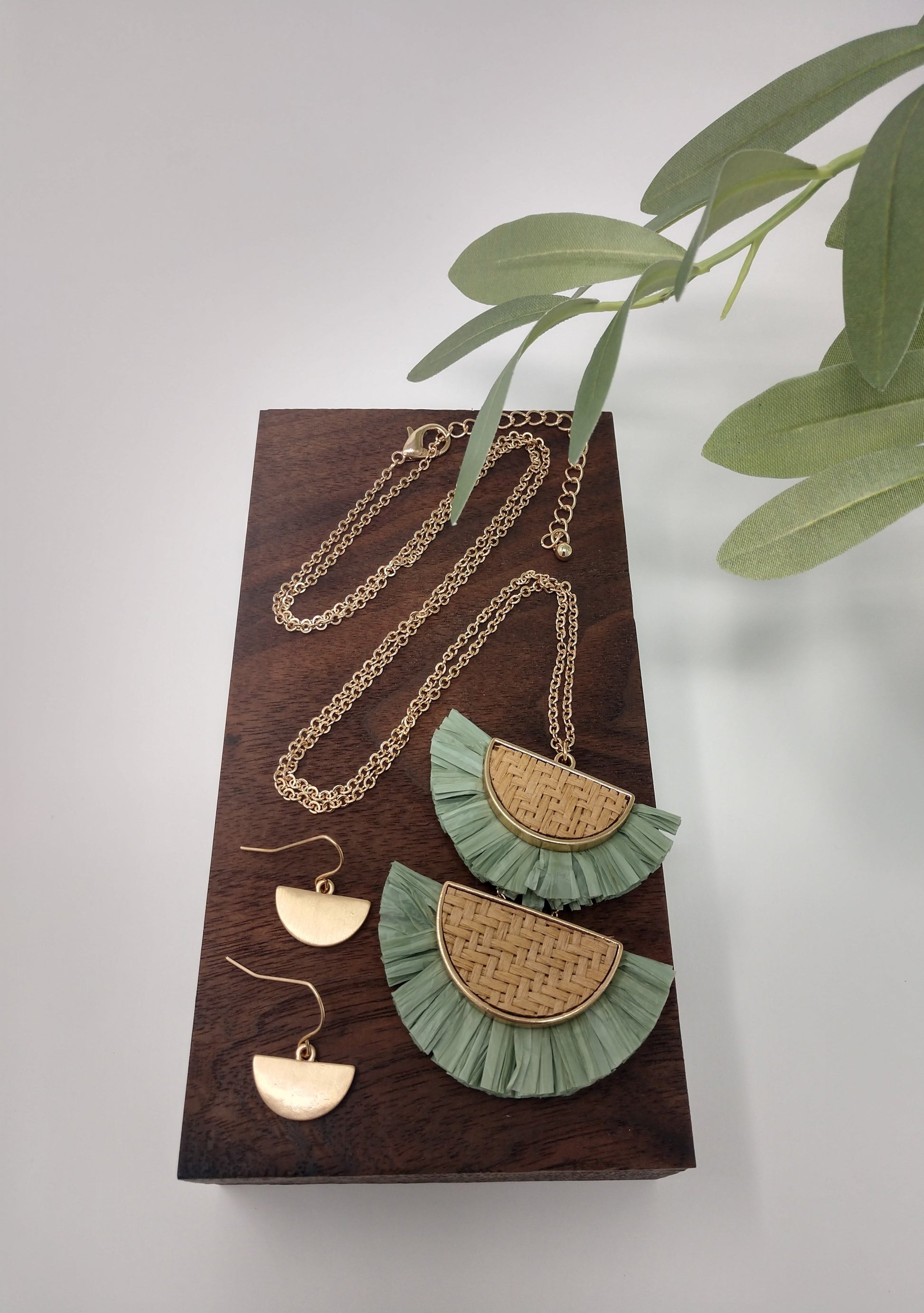 It is a 30" long gold tone necklace with a 3" extender and lobster claw closure. It is made with rattan, and raffia material. The pendant measures 2.5" and is so delicate feeling. Plus, it comes with the most perfect set of earrings. They are .75" fish hook style with a .25 drop. Fashion jewelry is a great way to add affordable fun, colorful, trendy pieces to your collection. 