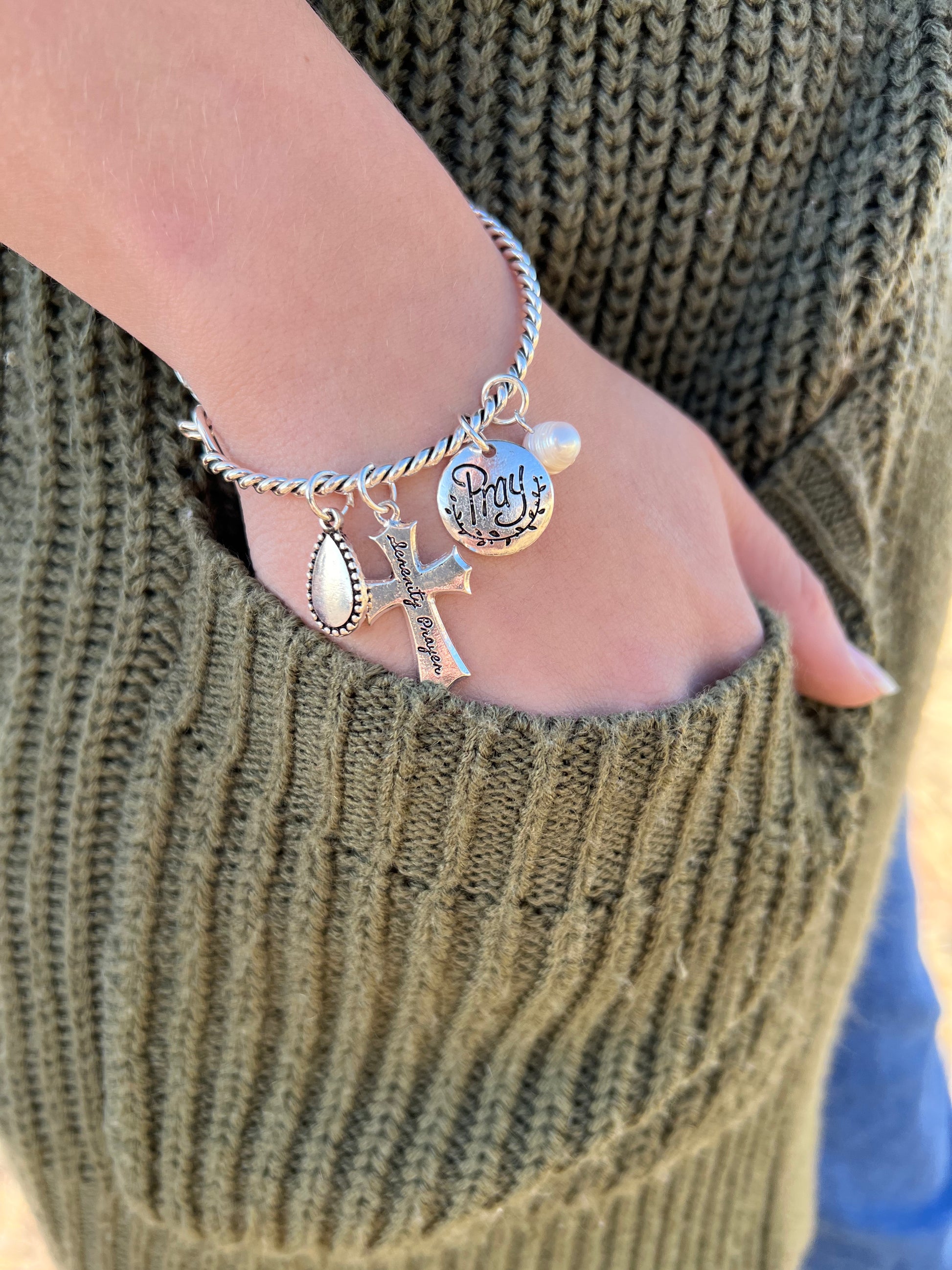 This bangle bracelet is made of a twisted silver tone band a 1.25" serenity prayer cross, .75" Pray disc charm, .75" teardrop charm, .5" faux pearl charm. It measures approximately 2"-2.5" in diameter. They close with a well designed hook closure. 